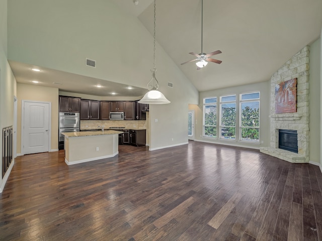 unfurnished living room with dark wood-type flooring, ceiling fan, a stone fireplace, sink, and high vaulted ceiling