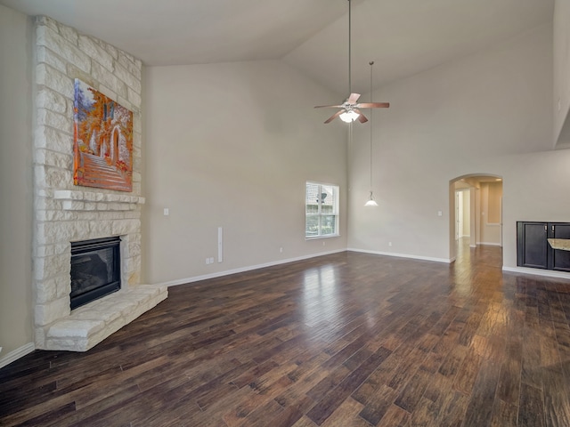 unfurnished living room with a stone fireplace, ceiling fan, dark hardwood / wood-style flooring, and high vaulted ceiling