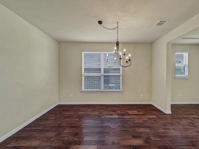 spare room featuring dark wood-type flooring and an inviting chandelier