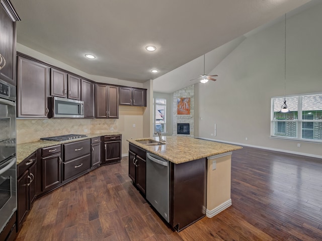 kitchen featuring appliances with stainless steel finishes, a fireplace, decorative backsplash, dark wood-type flooring, and ceiling fan