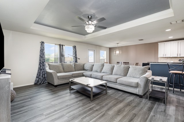 living room with ornamental molding, ceiling fan with notable chandelier, a tray ceiling, and dark wood-type flooring