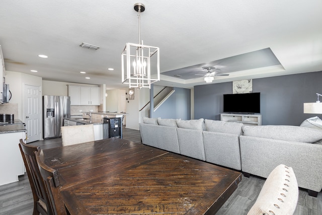 dining space with a tray ceiling, sink, dark hardwood / wood-style floors, and ceiling fan with notable chandelier