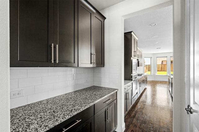 kitchen with dark brown cabinetry, decorative backsplash, dark hardwood / wood-style flooring, and light stone counters