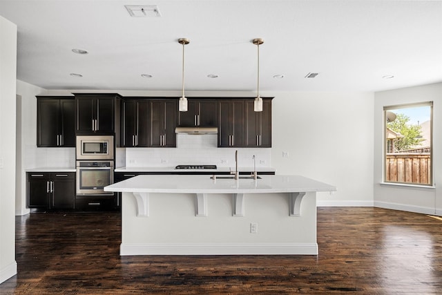 kitchen with sink, an island with sink, decorative light fixtures, a breakfast bar, and appliances with stainless steel finishes