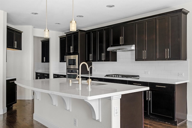 kitchen with stainless steel appliances, a kitchen island with sink, sink, decorative light fixtures, and dark hardwood / wood-style floors