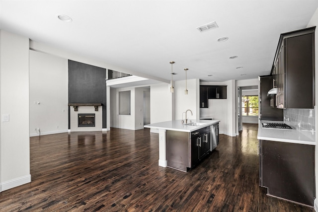 kitchen with sink, hanging light fixtures, tasteful backsplash, dark hardwood / wood-style flooring, and a center island with sink