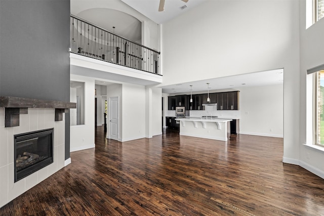 unfurnished living room featuring a towering ceiling, ceiling fan, dark wood-type flooring, sink, and a fireplace