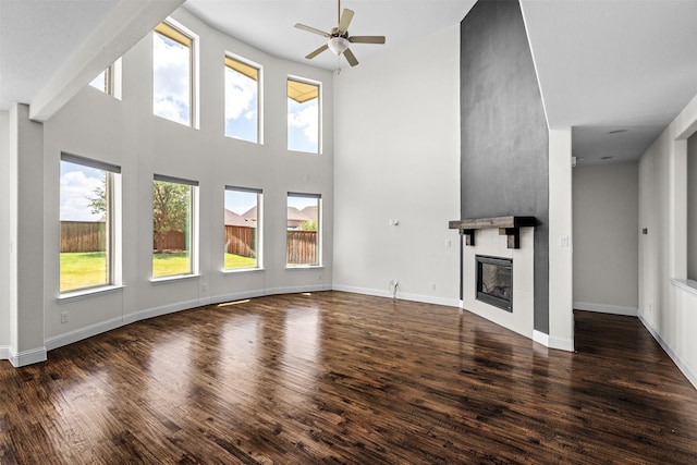 unfurnished living room featuring ceiling fan, a large fireplace, a towering ceiling, and dark wood-type flooring