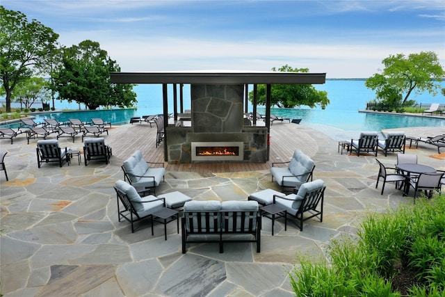 view of patio / terrace with an outdoor living space with a fireplace, a water view, and a community pool