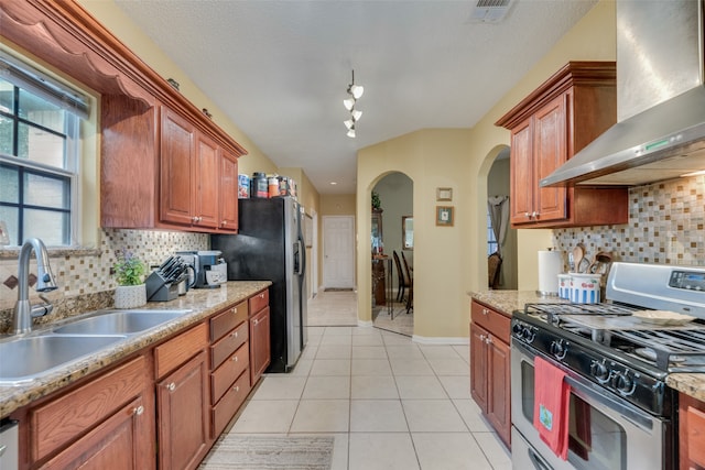 kitchen featuring wall chimney range hood, stainless steel gas range, tasteful backsplash, and light tile patterned floors