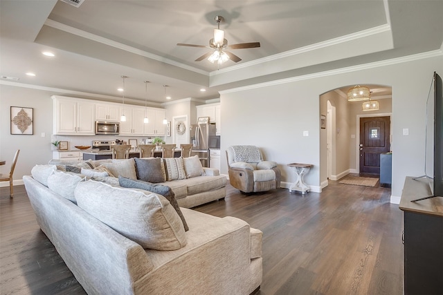 living room with ceiling fan, dark wood-type flooring, a raised ceiling, and ornamental molding