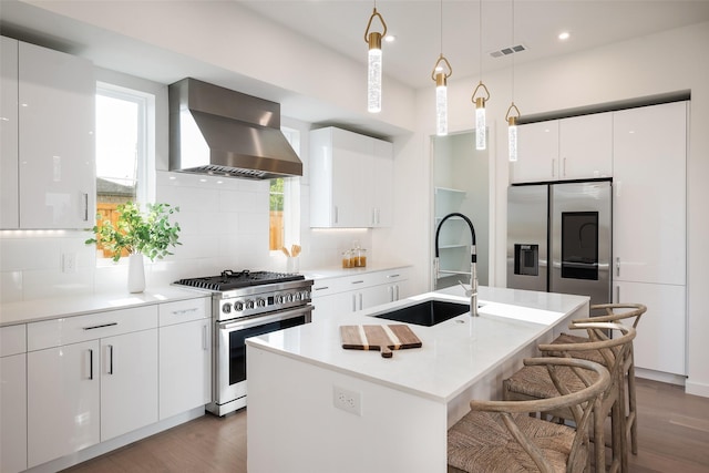 kitchen featuring appliances with stainless steel finishes, tasteful backsplash, wall chimney range hood, and a kitchen island with sink