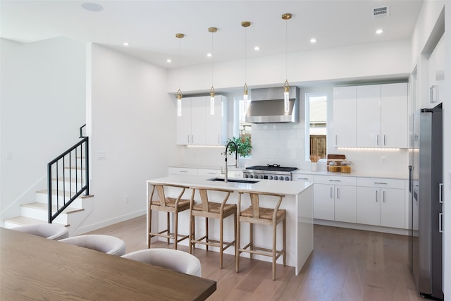 kitchen featuring white cabinetry, hardwood / wood-style floors, wall chimney exhaust hood, sink, and backsplash