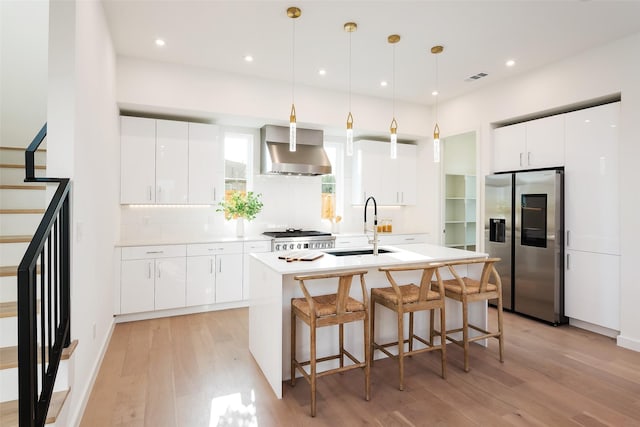 kitchen with white cabinets, stainless steel fridge, wall chimney range hood, sink, and light hardwood / wood-style floors