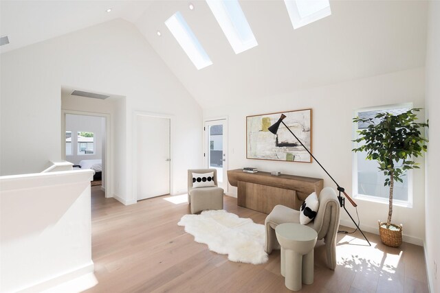 interior space with a skylight, high vaulted ceiling, and light wood-type flooring