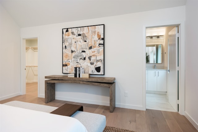 bedroom with a closet, ensuite bathroom, a spacious closet, and light wood-type flooring