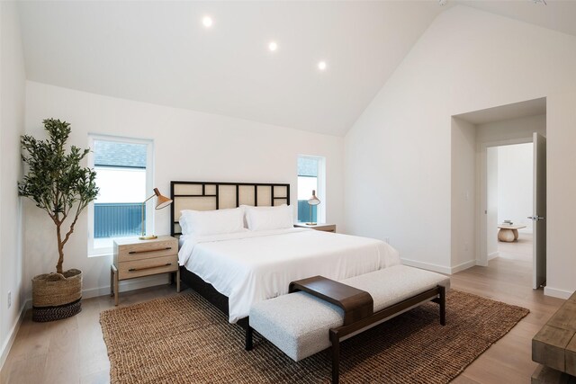 bedroom with high vaulted ceiling, multiple windows, and hardwood / wood-style flooring