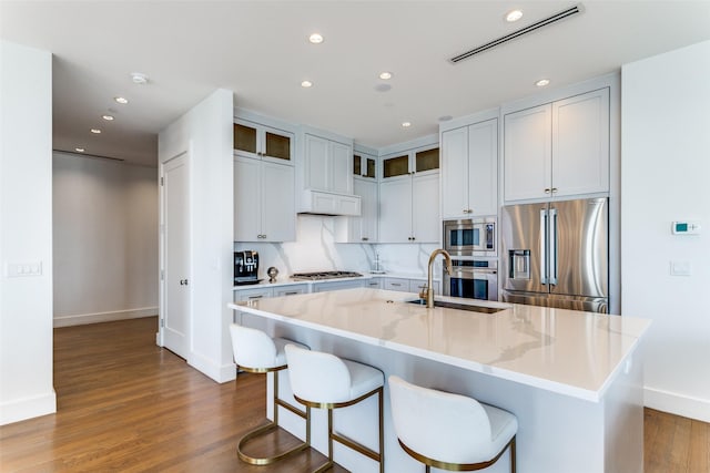 kitchen with light stone counters, sink, stainless steel appliances, and a kitchen island with sink