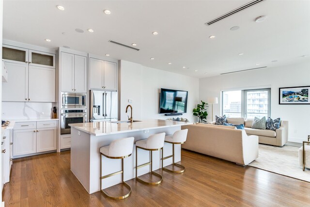 kitchen featuring sink, white cabinets, built in appliances, and an island with sink