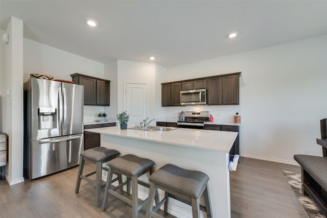 kitchen featuring an island with sink, light hardwood / wood-style floors, dark brown cabinetry, and appliances with stainless steel finishes