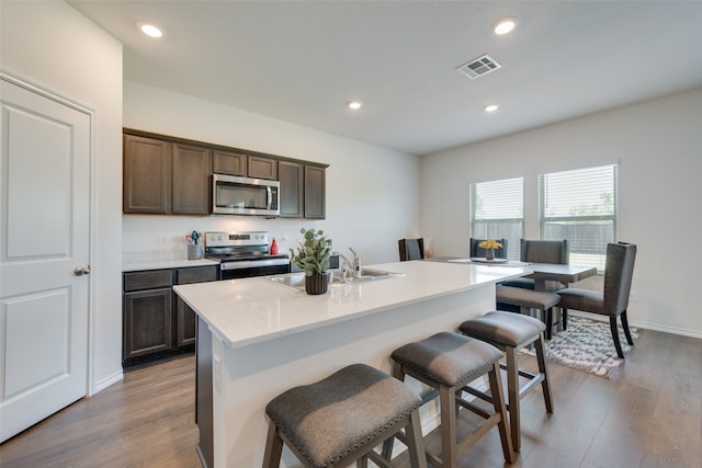 kitchen with an island with sink, hardwood / wood-style flooring, dark brown cabinets, and appliances with stainless steel finishes