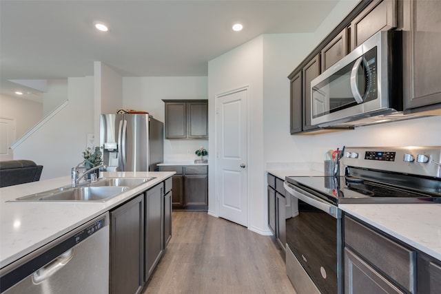 kitchen featuring stainless steel appliances, light hardwood / wood-style floors, sink, and light stone counters