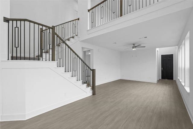 unfurnished living room featuring wood-type flooring, a towering ceiling, and ceiling fan