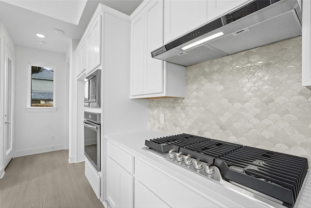 kitchen featuring white cabinetry, tasteful backsplash, light hardwood / wood-style flooring, stainless steel appliances, and exhaust hood