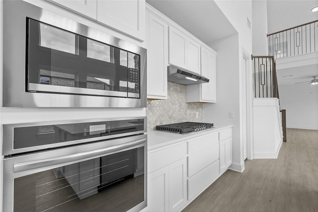 kitchen featuring ceiling fan, backsplash, stainless steel appliances, light hardwood / wood-style floors, and white cabinets