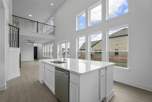 kitchen with sink, a kitchen island with sink, white cabinetry, light hardwood / wood-style floors, and stainless steel dishwasher