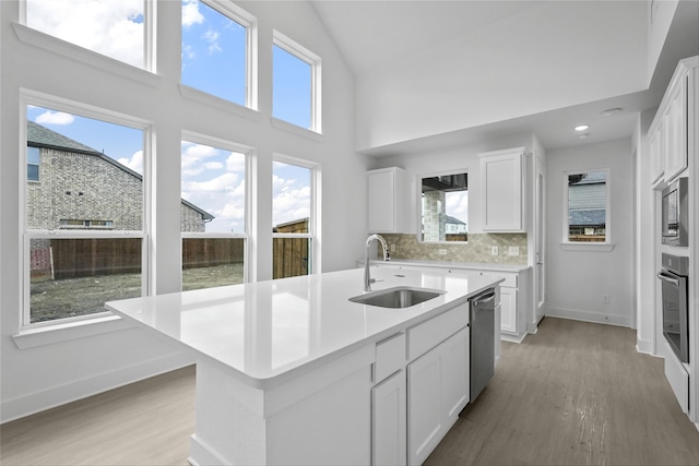 kitchen featuring tasteful backsplash, an island with sink, sink, white cabinets, and stainless steel appliances