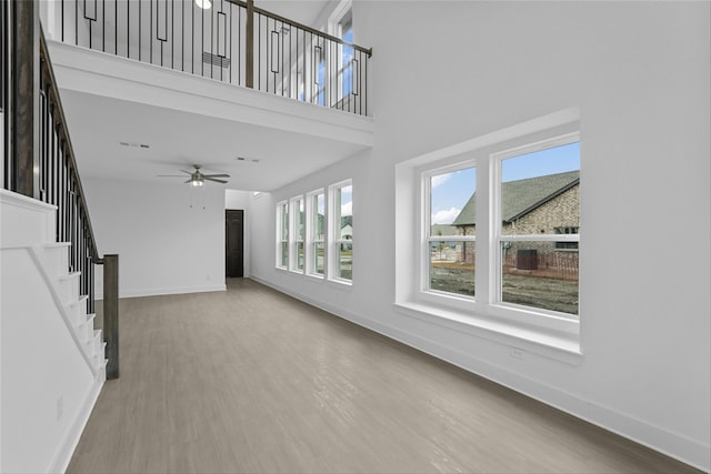 unfurnished living room with ceiling fan, hardwood / wood-style floors, and a towering ceiling