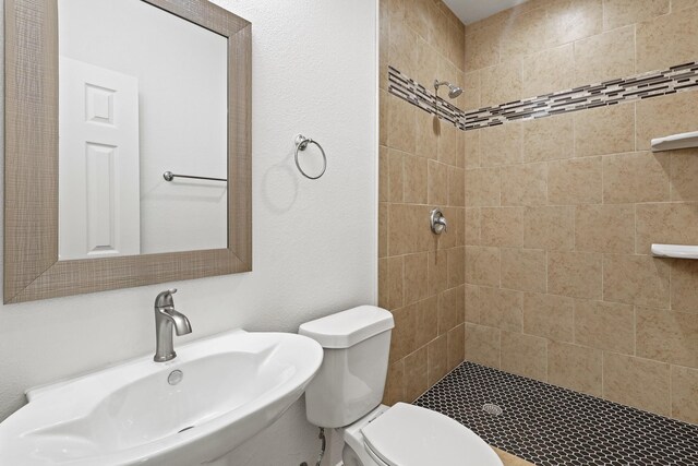 bathroom featuring a tile shower, sink, and toilet