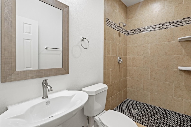 bathroom featuring sink, a tile shower, and toilet