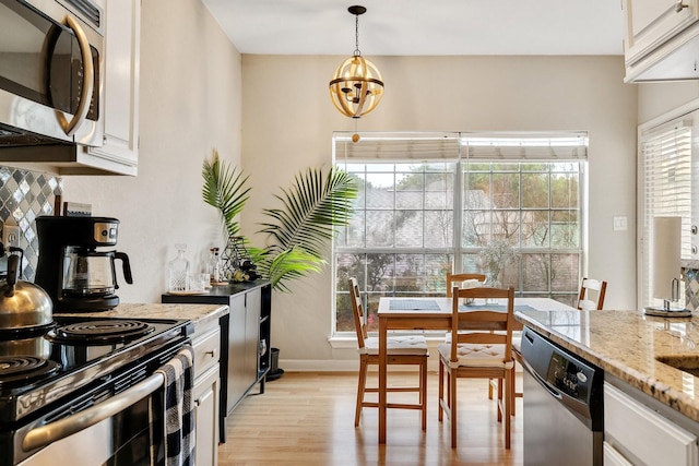 kitchen with a wealth of natural light, appliances with stainless steel finishes, pendant lighting, white cabinetry, and light stone counters