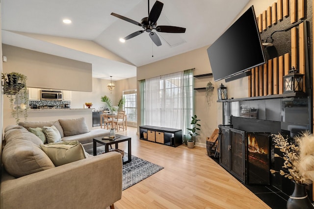 living room featuring ceiling fan, vaulted ceiling, a tiled fireplace, and light wood-type flooring