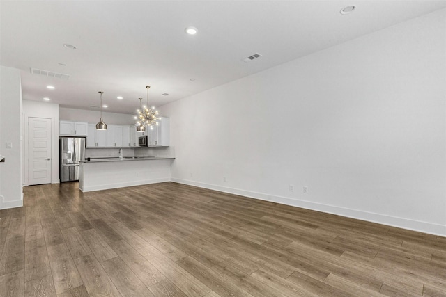 unfurnished living room featuring a chandelier, visible vents, and wood finished floors