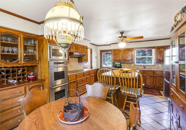 tiled dining area with ceiling fan with notable chandelier, a sink, and crown molding