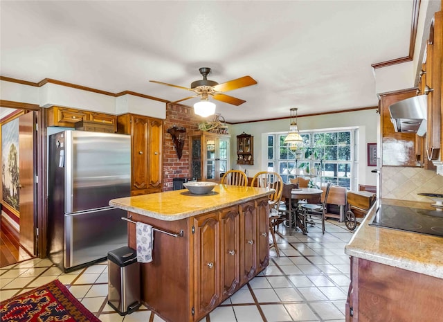 kitchen featuring wall chimney exhaust hood, brown cabinets, freestanding refrigerator, hanging light fixtures, and backsplash