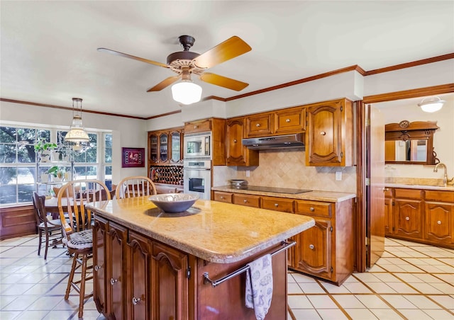 kitchen featuring under cabinet range hood, stainless steel appliances, a sink, a kitchen island, and pendant lighting