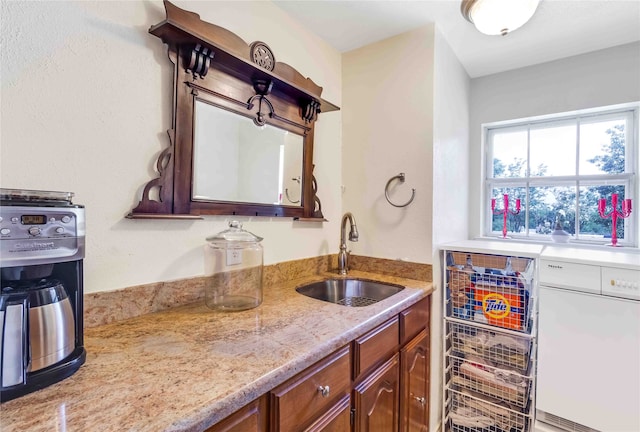 kitchen featuring dishwasher, light stone counters, and a sink