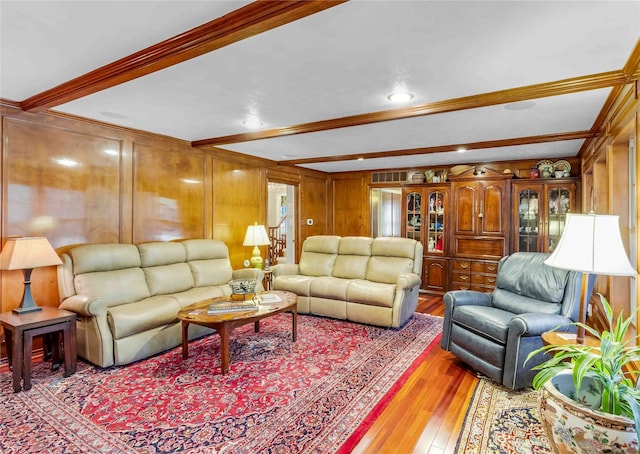 living area with ornamental molding, beam ceiling, and wood finished floors