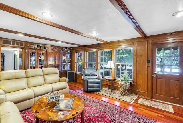 living room with a textured ceiling, wood finished floors, visible vents, beamed ceiling, and crown molding