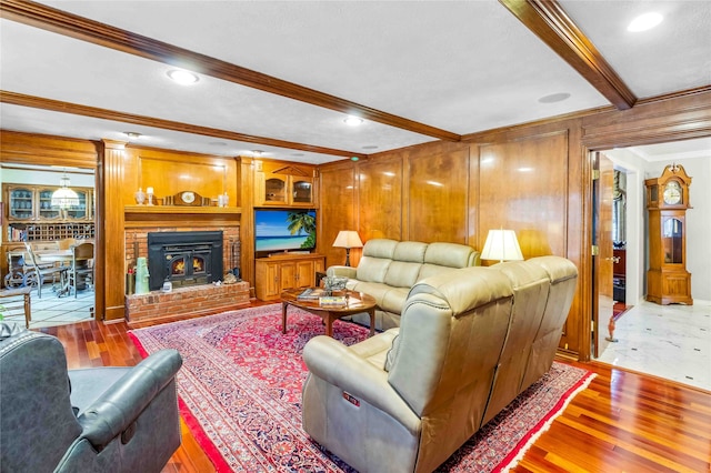 living area featuring ornamental molding, light wood-style flooring, beam ceiling, and wooden walls