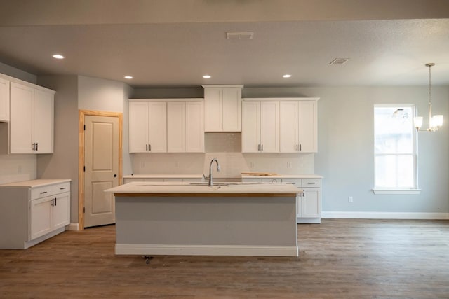 kitchen with hardwood / wood-style flooring, a kitchen island with sink, and white cabinets