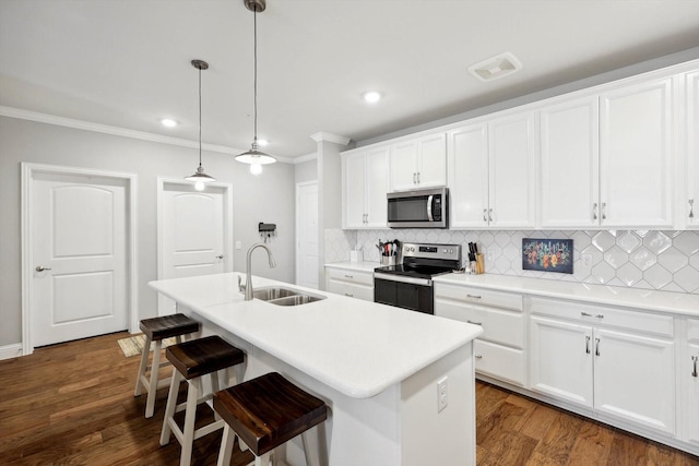 kitchen with white cabinets, appliances with stainless steel finishes, decorative light fixtures, sink, and a kitchen island with sink