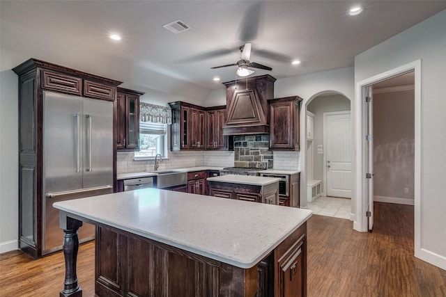 kitchen with appliances with stainless steel finishes, sink, custom exhaust hood, a center island, and dark brown cabinets