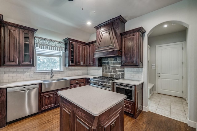 kitchen featuring sink, premium range hood, stainless steel appliances, dark brown cabinetry, and a kitchen island