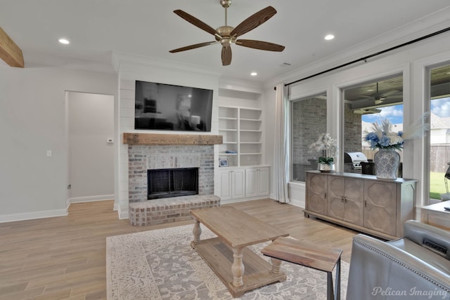 living room featuring ceiling fan, a brick fireplace, ornamental molding, built in shelves, and light hardwood / wood-style floors