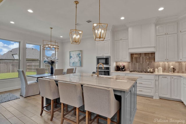 kitchen with light hardwood / wood-style floors, light stone counters, stainless steel appliances, and an island with sink